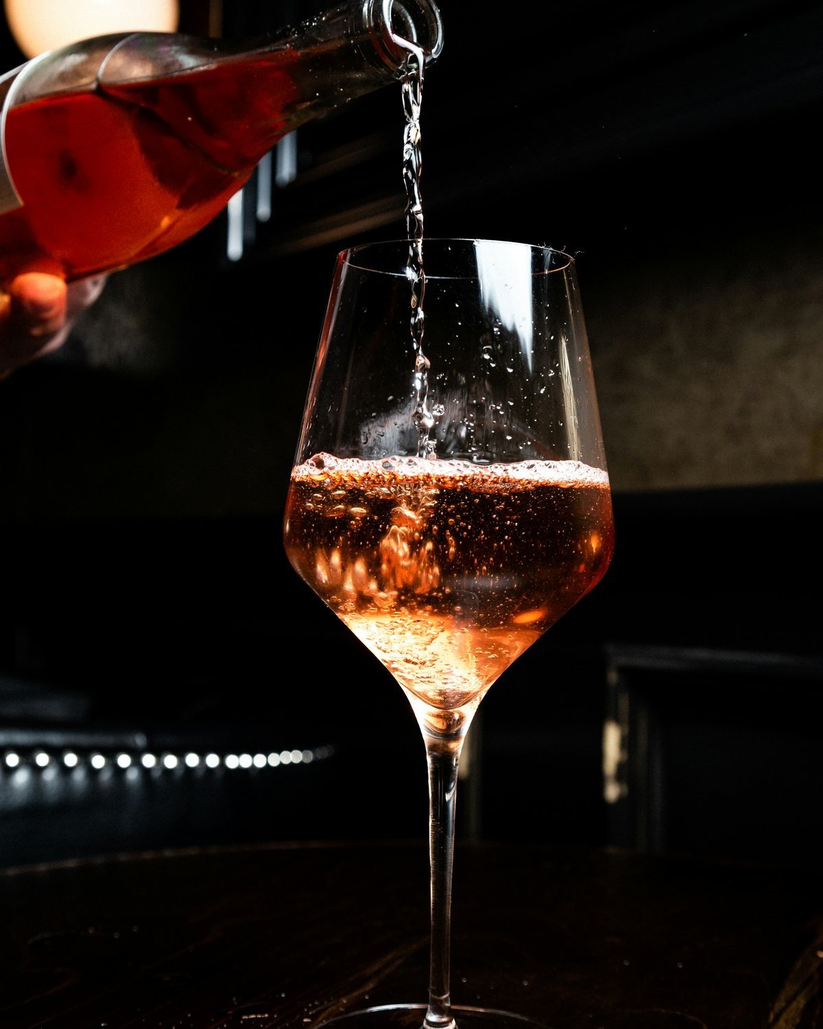 Servido de vino rosado en una copa a contraluz sobre una barra oscura