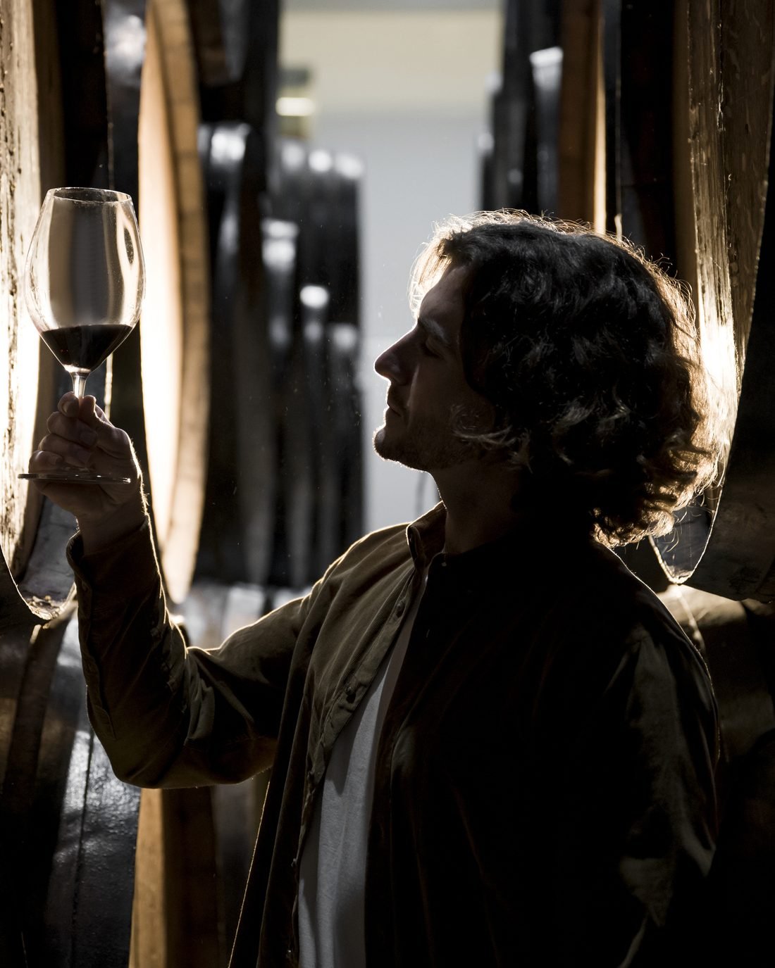 Sumiller observando a contraluz el color de una copa de vino tinto en una bodega